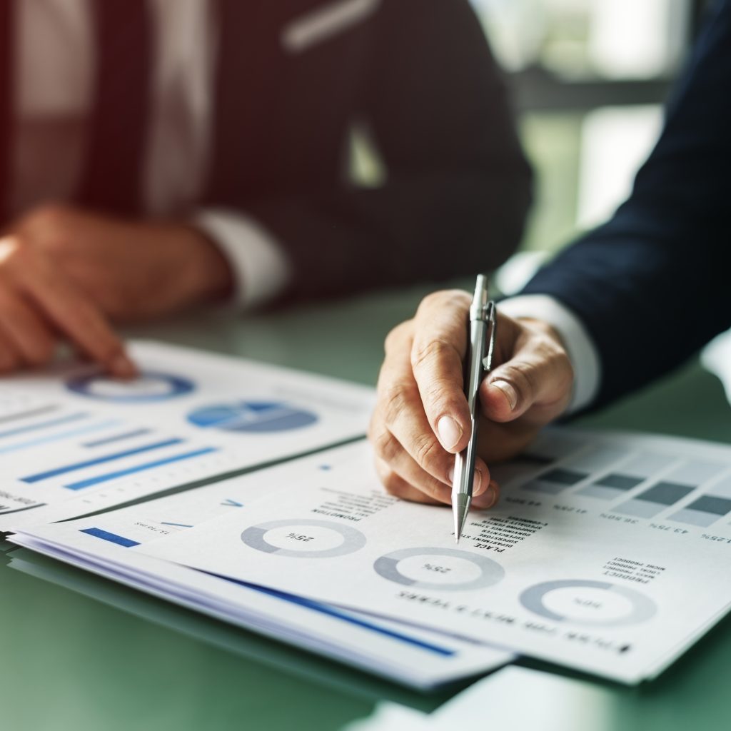 Hands writing business documents on a desk with a laptop and office supplies